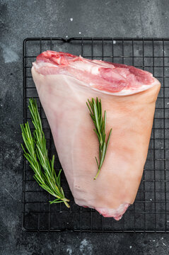 Raw pork knuckle on cooling rack with rosemary on dark stone surface perfect for cooking guides butchery visuals and recipe content.