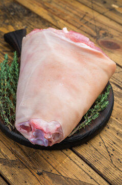 Uncooked pork shank hamhock showing skin texture fat layers and structural anatomy on wooden surface with herbs for technical food photography.