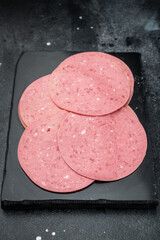Thin round slices of Turkish beef salam arranged on a slate board with red pepper on dark stone background ideal for deli and food stock use © Mironov