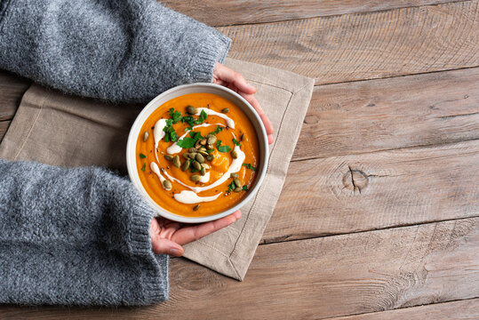 Female hands in knitted sweater holding bowl with pumpkin soup