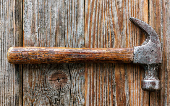 single vintage hammer lying on a rustic wooden floor, worn wooden handle with metal head showing signs of use, soft natural window light casting subtle shadows