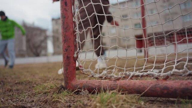 player scores amidst urban goal attempt, striker scores as goalie reacts in city environment, urban soccer moment where player scores goal with goalkeeper and post witnessing silently