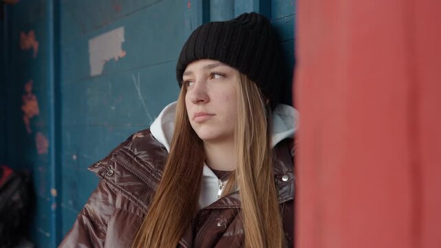 young woman relaxes outdoors amid snowy tranquility, teen girl enjoys quiet and peaceful winter outdoor break, youthful female rests peacefully against shelter wall amid serene winter landscape