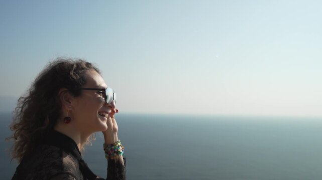 Woman sunglasses seaside traveler looks out over the vast blue ocean enjoying the scenic view on a sunny summer day.