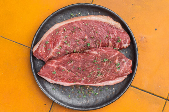 Raw rump cap beef steaks also known as top sirloin cap with thyme and salt on black plate, yellow background