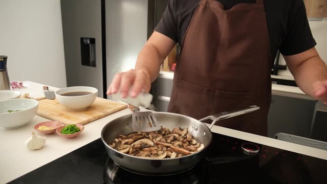 Male cook preparing a mushroom dish on an induction hob in a modern kitchen