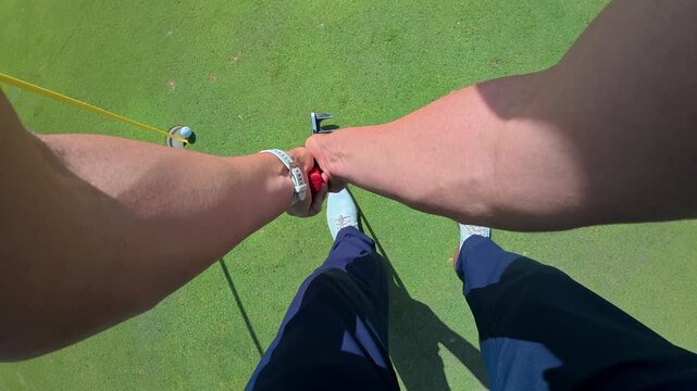 Player's perspective of a professional golfer successfully putting a golf ball into the hole on a sunny day, showcasing skill and precision on the manicured green during a competitive match