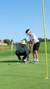 Professional golf coach teaching a young student how to putt correctly on the green, explaining the technique and aiming for the hole on a sunny day at the golf course