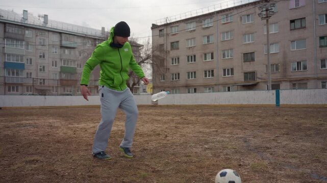 caucasian man practicing street kicking drills on brown field, explosive footwork and technique in green jacket, focused strike sequences and athletic training in urban neighborhood