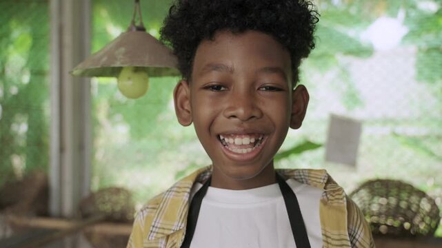 Portrait of happy cute African child boy standing smiling and laughing with fun and enjoying while looking at camera in henhouse at organic farm. Black children learning agriculture lesson in school. 