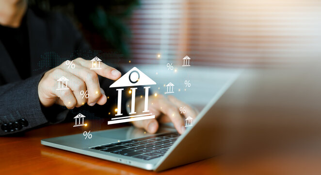 Businessman pointing at virtual bank building and percentage icons interface on screen with laptop. Concept of banking, online finance, interest rates, investment, and digital financial services.