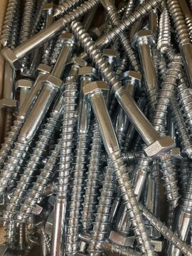 Close-up of a large pile of metal hex head screws with coarse threads, creating a detailed industrial background for construction, hardware, engineering and manufacturing concepts.