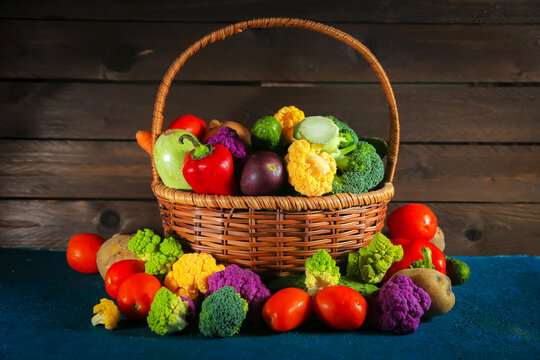 Fresh, shiny vegetables of various varieties in a wicker basket on a wooden background.