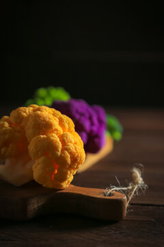 Multicolored cauliflower on a wooden table. Purple, yellow, and green florets.