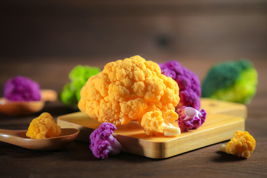 Multicolored cauliflower on a wooden table. Purple, yellow, and green florets.