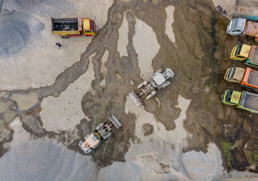 Aerial Scenery of Wheel Loader and Several Haul Trucks Working in a Rock and Sand Quarry with Distinctive Ground Patterns, Industrial Mining Site view from above.