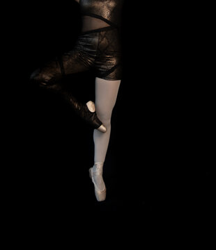 Dancer in black outfit performing a ballet pose in a dark studio setting