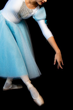 Child performing ballet dance in light blue costume on stage with dark background
