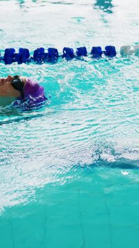 Swimmer glides smoothly on backstroke through clear turquoise water. Blue lane dividers mark pool's lanes. Ripples flow around swimmer's head. Movement creates gentle water disturbance