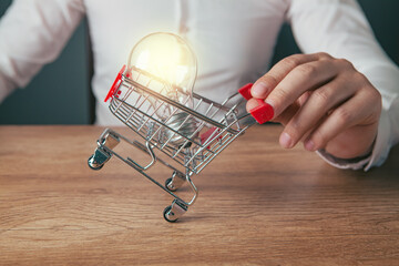 man hand holding shopping cart with lightbulb on wooden table background. © Artvibe