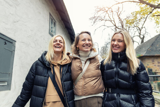 Cheerful friends laugh together on autumn city walk, sharing hugs and joyful travel moments. Candid group portrait captures friendship, reunion, happiness, leisure and weekend adventure outdoors