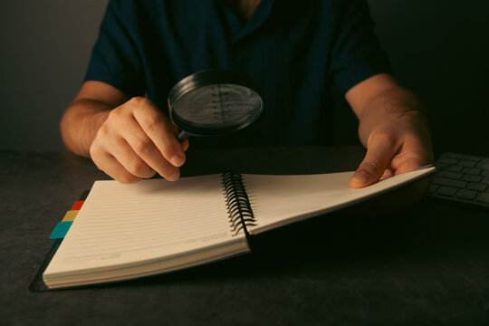 Man looking through a magnifying glass at a notebook on a dark background