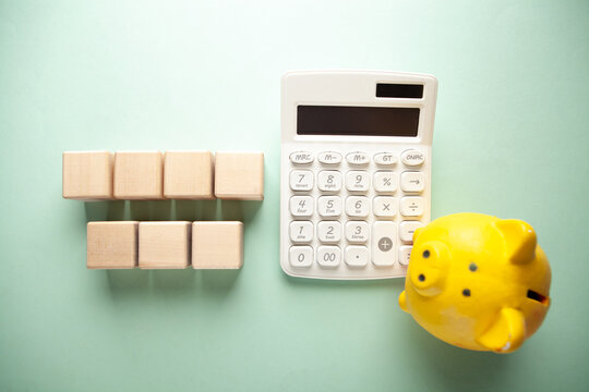 Calculator, piggy bank and wooden cubes on green background