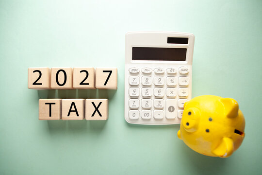 Calculator, piggy bank and wooden cubes with text 2027 tax