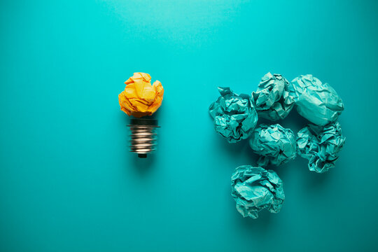 Incandescent light bulb and crumpled paper balls on blue background