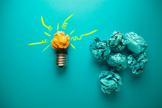 Incandescent light bulb and crumpled paper balls on blue background