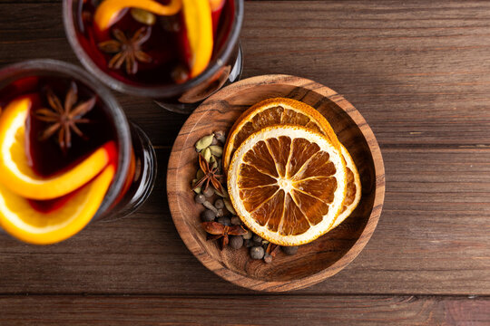 Warm mulled wine drink with spices and dried orange slices served in a wooden bowl on a rustic table