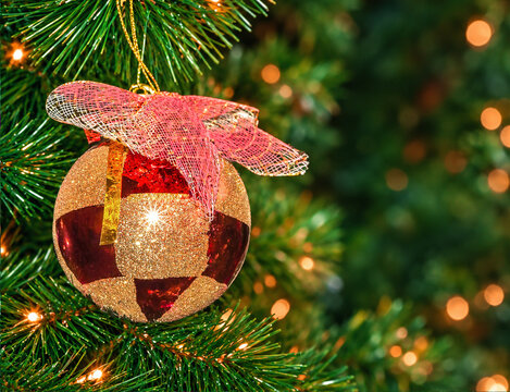 Red and Gold Glitter Christmas Bauble with Ribbon Bow on Fir Tree