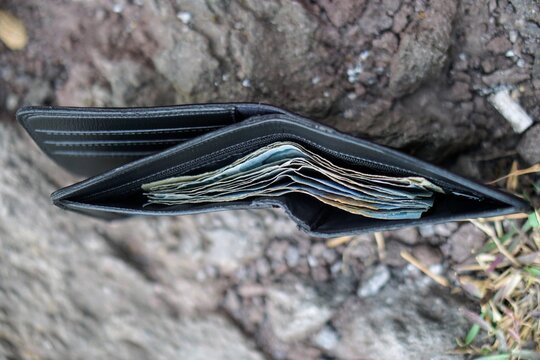 An open black leather wallet filled with Indonesian Rupiah banknotes lying on a rocky ground texture, illustrating concepts of lost wallet, personal finance, and limited