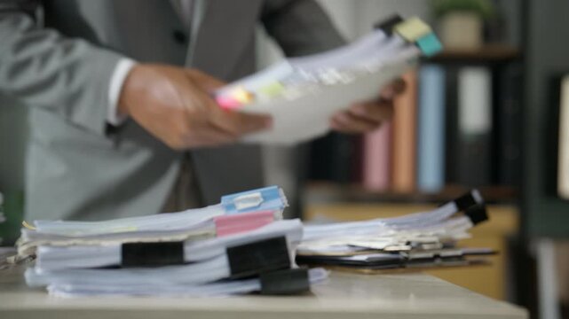Businessman Sorting Paperwork and Files at Busy Corporate Office