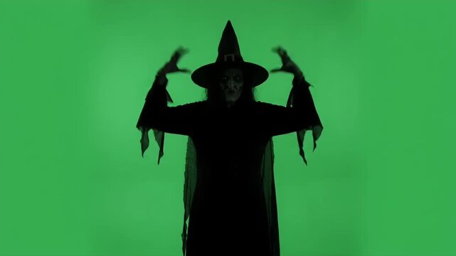 Silhouette of Wicked Witch Cackling on Green Screen - A menacing, silhouetted witch with a pointed hat cackles with a creepy grin and raises her hands with claw-like fingers.