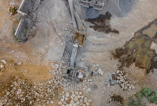 Rock Crusher Machinery Near Large Boulders and Split Rocks and Wet Ground Areas at an Industrial Quarry Site, Industrial Mining Site view from above.