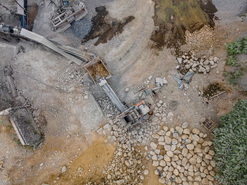 Rock Crusher Machinery Near Large Boulders and Split Rocks and Wet Ground Areas at an Industrial Quarry Site, Industrial Mining Site view from above.