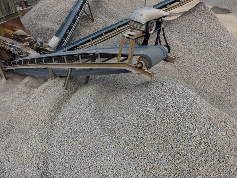 Multiple Conveyor Belt Systems and Large Aggregate Stockpiles at an Industrial Quarry Facility. Rock Processing and Bulk Aggregate Transportation, Industrial Mining Site view from above.