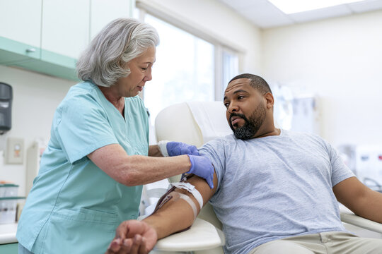 Senior phlebotomist drawing blood from a male patient's arm in a bright clinic