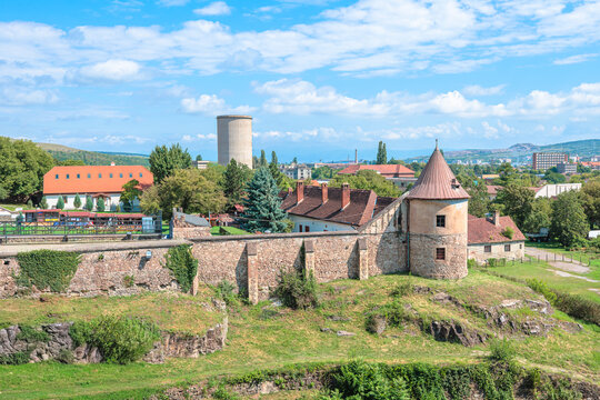 Corvin Castle, a historical landmark and Gothic-Renaissance fortress, showcasing its stone walls and tower against a backdrop of trees and town buildings under a clear sky in Transylvania, Romania