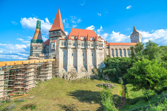 Corvin Castle, a significant gothic-renaissance architectural masterpiece in Hunedoara, Romania, undergoing partial renovation with scaffolding against a vibrant blue sky during a day in Transylvania