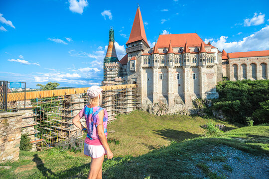 Woman standing admiring the impressive Corvin Castle, a significant gothic-renaissance landmark undergoing reconstruction in Hunedoara, Romania, on a clear sunny day in Transylvania