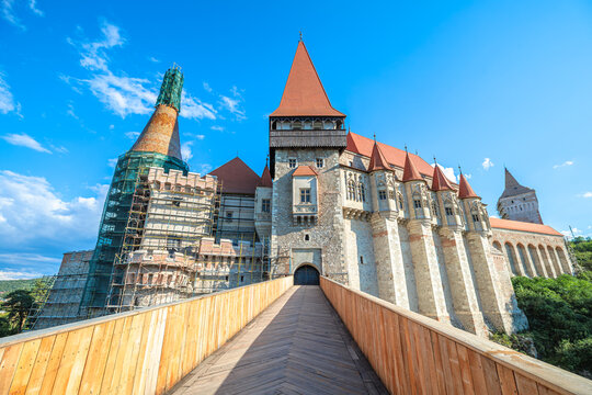 Corvin Castle, a significant Gothic-Renaissance landmark in Transylvania, Romania, stands under a clear blue sky, presenting its architectural grandeur and ongoing restoration work on prominent tower