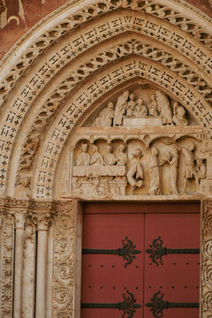Ornate red wooden church door with forged iron hinges under gothic carved stone tympanum in Rouen, France