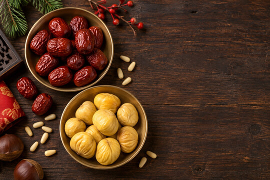 Dried jujubes and chestnuts in brass bowls on dark wood