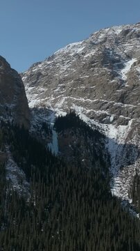 Scenic winter landscape footage of rugged rocky mountains with snow patches and dense conifer forest in Barskoon Gorge, Issyk-Kul Region, Kyrgyzstan