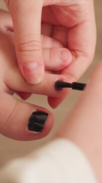Close up shows person carefully painting their own cuticles with dark colored varnish. focus remains steady throughout as hands and nail polish brush interact emphasizing meticulous