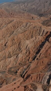 Drone footage of Skazka Canyon with layered red sandstone ridges and deep ravines near Issyk-Kul Lake, Kyrgyzstan on a clear sunny day
