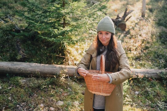 Woman holding a wicker basket while searching for wild mushrooms in a sunlit forest, illustrating mushroom picking, seasonal foraging, nature walks and slow outdoor living.