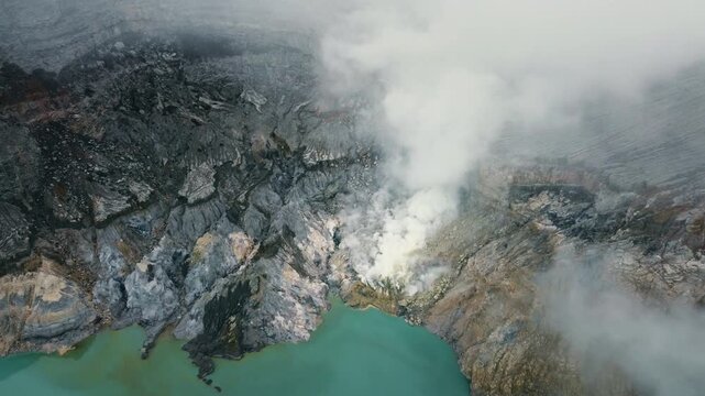 Turquoise Kawah Ijen crater lake borders steaming sulfur vents as volcanic gas drifts through the rugged caldera in Indonesia.